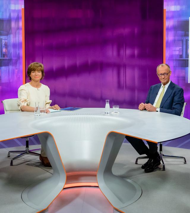 Moderatorin Maybrit Illner und Bundeskanzler Friedrich Merz schauen lächelnd in die Kamera