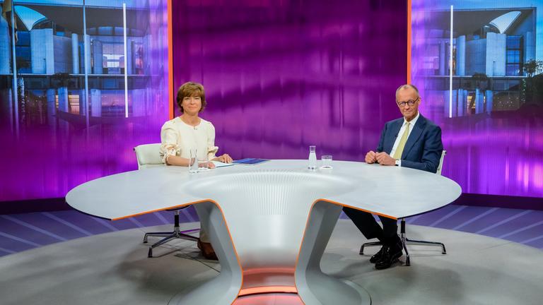 Moderatorin Maybrit Illner und Bundeskanzler Friedrich Merz schauen lächelnd in die Kamera
