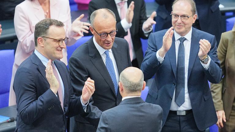 Der scheidende Bundeskanzler Olaf Scholz (M, von hinten, SPD) gratuliert dem neu gewählten Bundeskanzler Friedrich Merz (M, CDU) zu seiner Wahl. im Bundestag.