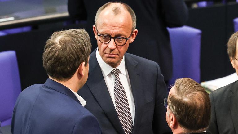 Der Partei- und Fraktionsvorsitzende der Christlich Demokratischen Union (CDU), Friedrich Merz (M.), spricht mit dem Ko-Vorsitzenden der Sozialdemokratischen Partei (SPD), Lars Klingbeil (L.), während einer Sonderplenarsitzung des Deutschen Bundestages am 18. März 2025 in Berlin. 