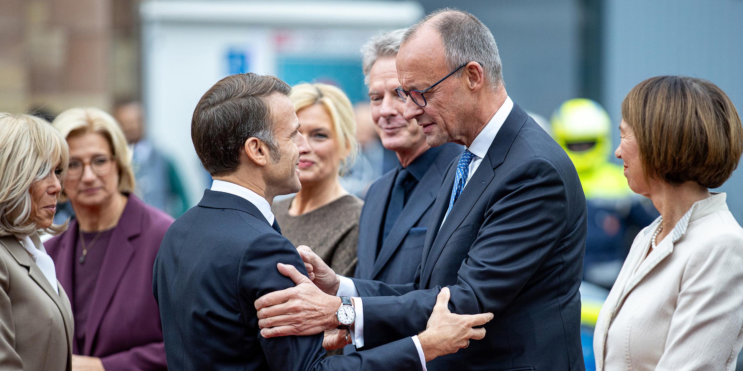  Frankreichs Präsident Emmanuel Macron (M.l) begrüßt Bundeskanzler Friedrich Merz (CDU) bei seiner Ankunft vor der saarländischen Staatskanzlei während der zentralen Feierlichkeiten dem Tag der Deutschen Einheit, Brigitte Macron, Anke Rehlinger (SPD), saarländische Ministerpräsidentin und Bundesratspräsidentin, Bundestagspräsidentin Julia Klöckner (CDU) und ihr Partner, der Fernsehmoderator Jörg Pilawa, sowie Charlotte Merz, Frau des Bundeskanzlers, sehen zu.