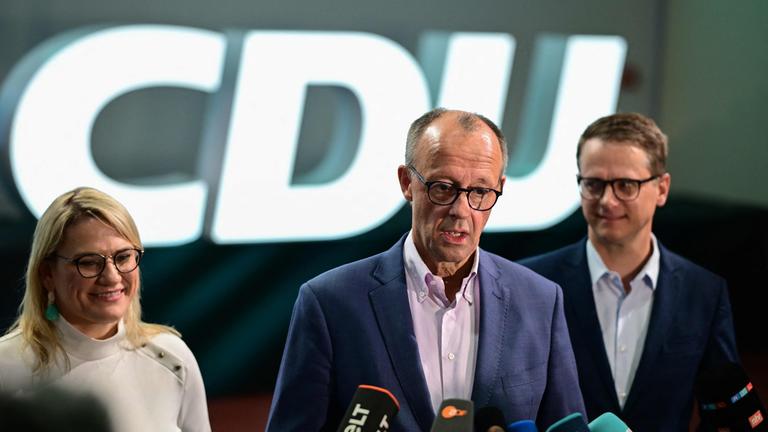 Friedrich Merz in der Mitte an einem Mikrofon. Carsten Linnemann und Christina Stumpp stehen neben ihm.