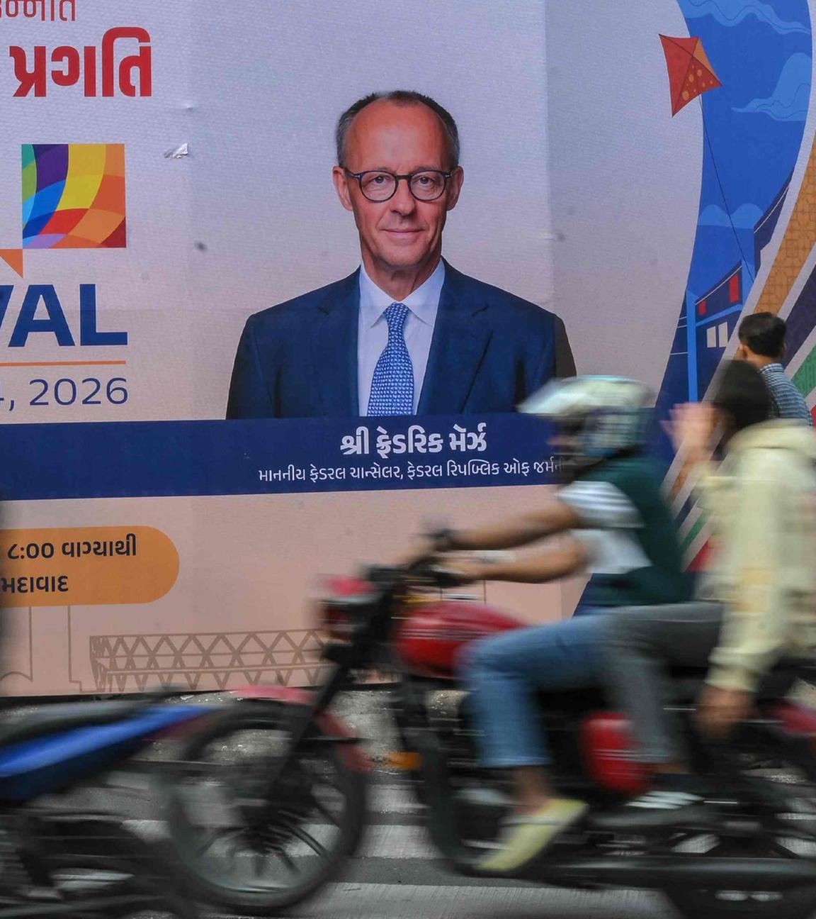 Motorradfahrer passieren in Ahmedabad am 8. Januar 2026 eine Werbetafel mit Fotos von Deutschlands Bundeskanzler Friedrich Merz (r.) und Indiens Premierminister Narendra Modi anlässlich des bevorstehenden Indien-Besuchs von Merz.