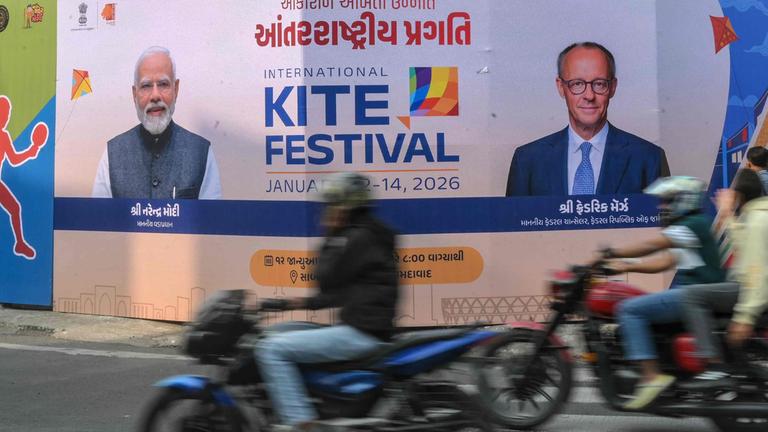 Motorradfahrer passieren in Ahmedabad am 8. Januar 2026 eine Werbetafel mit Fotos von Deutschlands Bundeskanzler Friedrich Merz (r.) und Indiens Premierminister Narendra Modi anlässlich des bevorstehenden Indien-Besuchs von Merz.