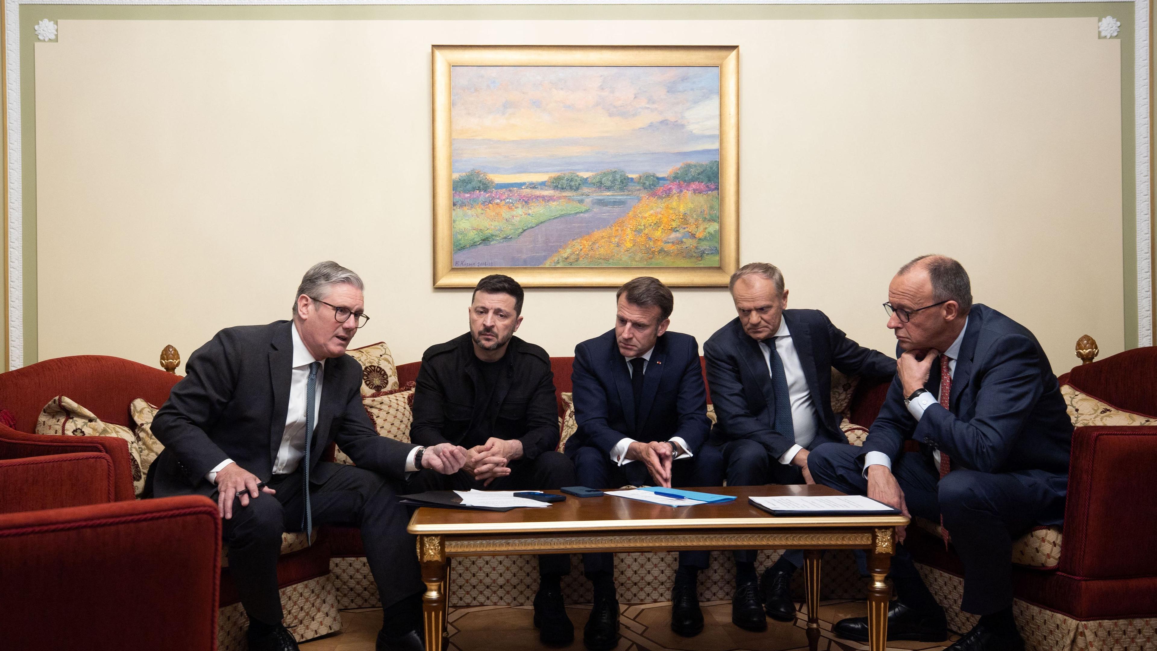 Der britische Premier Starmer, der ukrainische Präsident Selenskyj, der französische Präsident Macron, der polnische Premierminister Tusk und Bundeskantler Friedrich Merz sitzen zusammen um einen Tisch in Kiew.