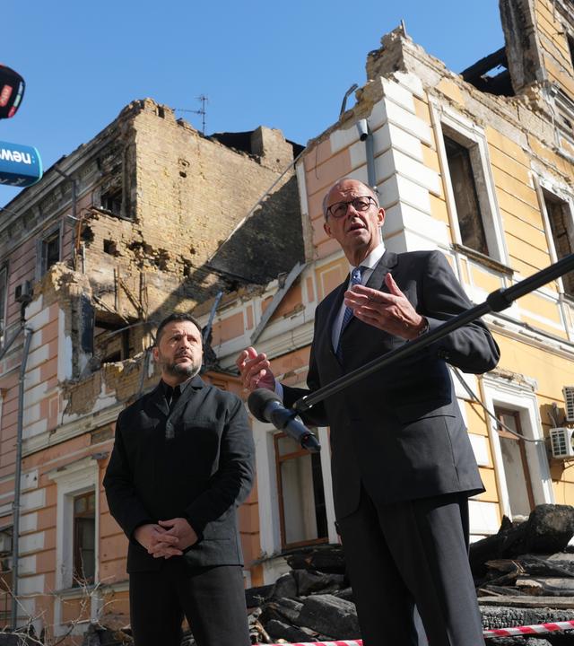 Der ukrainische Präsident Wolodymyr Selenskyj und der deutsche Bundeskanzler Friedrich Merz geben vor einem durch eine russische Drohne zerstörten Haus ein Pressestatement ab.