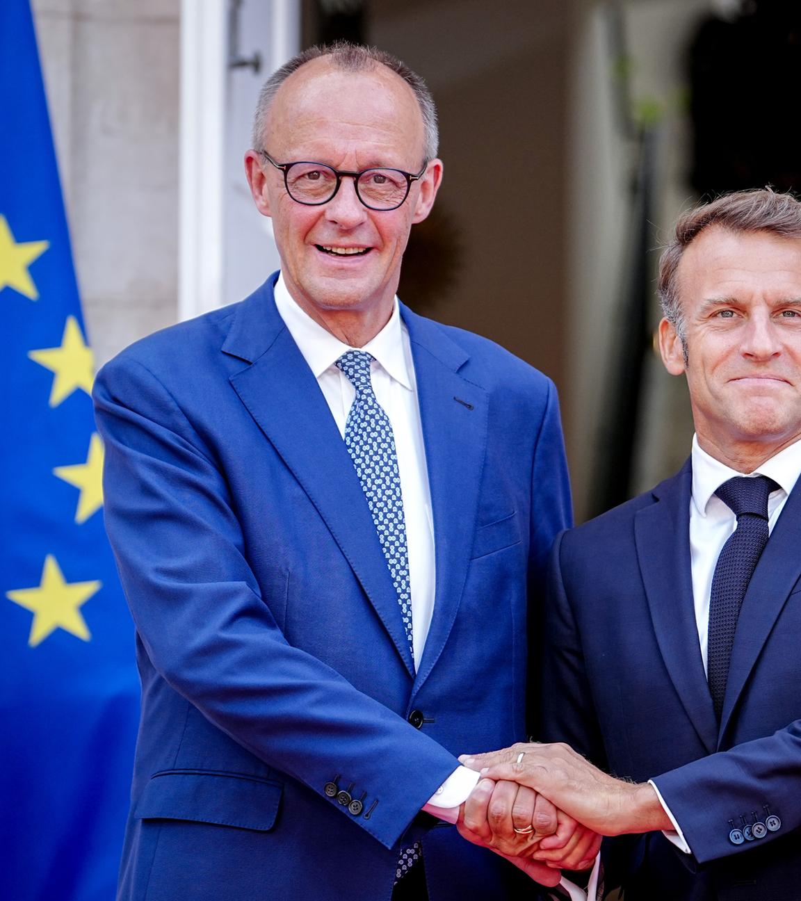 Bundeskanzler Friedrich Merz (l,CDU) und Frankreichs Präsident Emmanuel Macron begrüßen sich beim deutsch-französischen Regierungstreffen zur Wirtschafts- und Sicherheitspolitik.