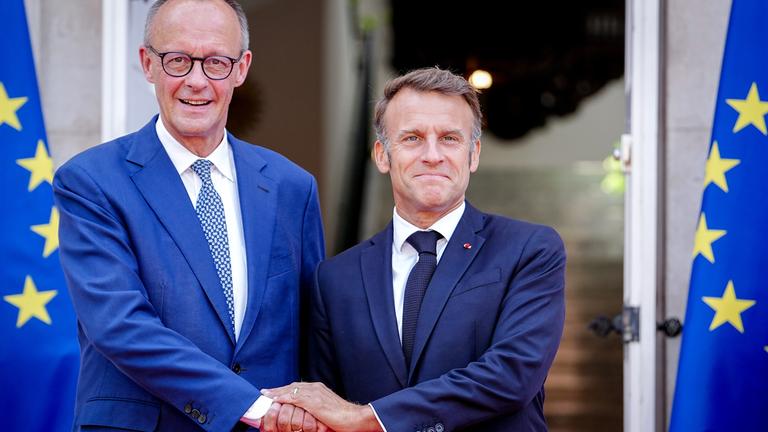 Bundeskanzler Friedrich Merz (l,CDU) und Frankreichs Präsident Emmanuel Macron begrüßen sich beim deutsch-französischen Regierungstreffen zur Wirtschafts- und Sicherheitspolitik.