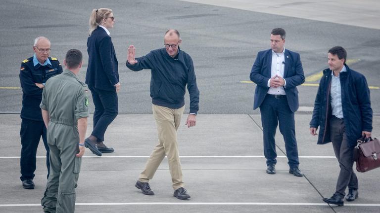 Merz kommt am Flughafen an und winkt