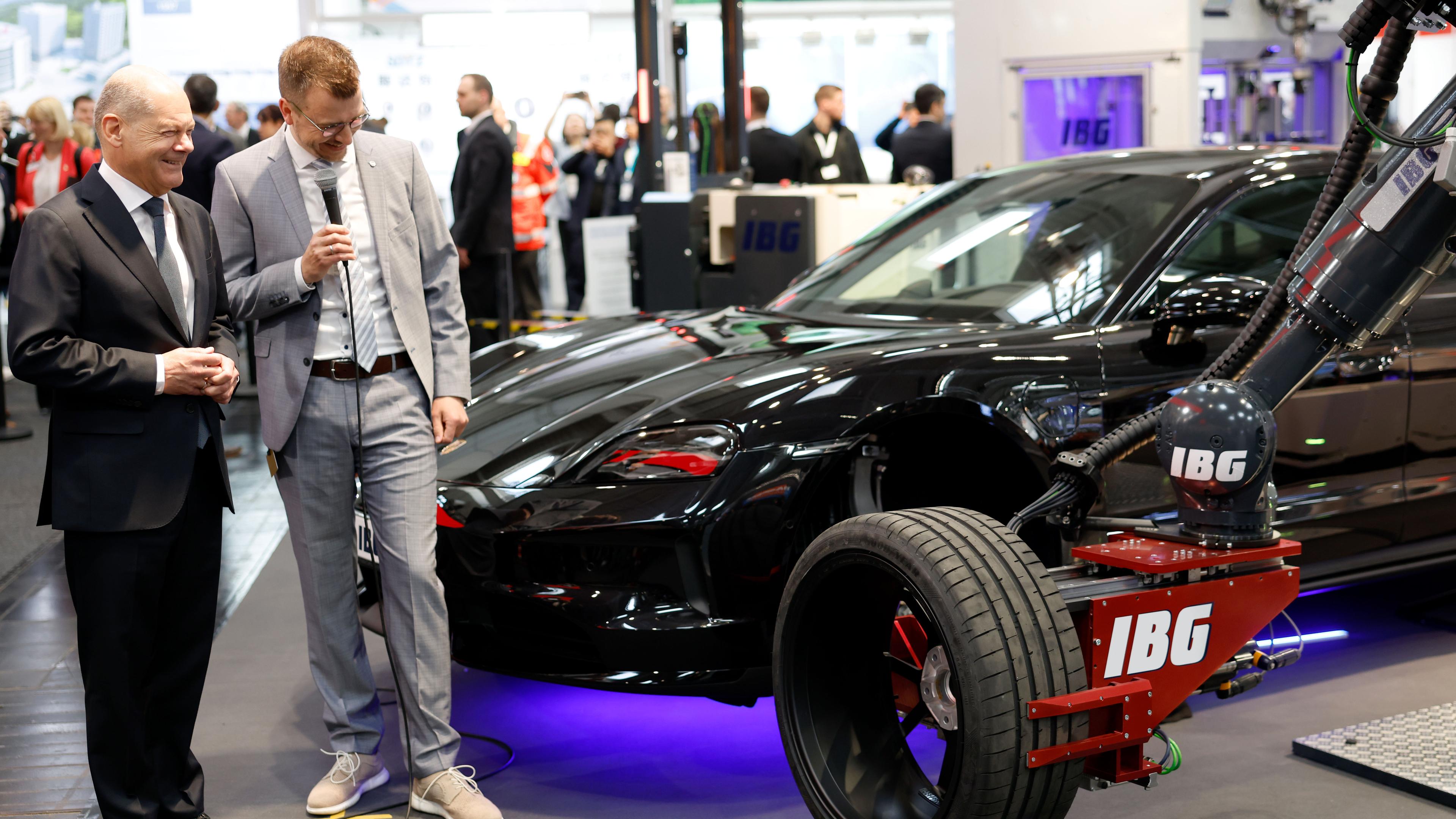 Matthias Fabian Goeke erklärt Olaf Scholz die vollautomatisierte Radmontage mit Roboterarm beim Eröffnungsrundgang auf der Industriemesse Hannover Messe 2025.