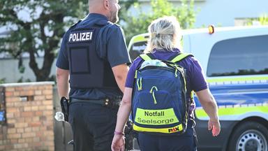 Ein Polzist und eine Notfallseelsorgerin stehen vor einem Einsatzfahrzeug.