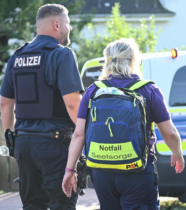 Ein Polzist und eine Notfallseelsorgerin stehen vor einem Einsatzfahrzeug.