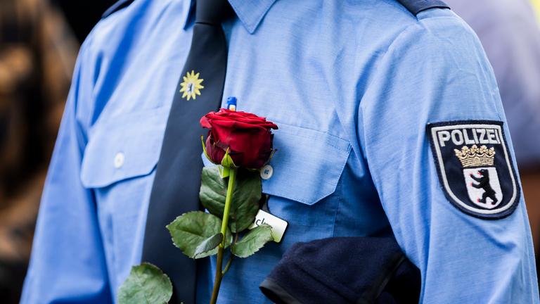 Ein Polizist hält bei einem Gedenken am Ende eines Schweigemarschs der «Blaulichtfamilie» von der Deutschen Polizeigewerkschaft (DPolG) und der Gewerkschaft der Polizei (GdP) an der Landesvertretung von Baden-Württemberg für den durch einen Messerangriff in Mannheim zu Tode gekommenen Polizisten eine Rose. 