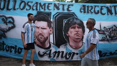 Zwei Argentinien-Fans gehen in Miami Beach an einem Plakat vorbei, auf dem die Konterfeis von Lionel Messi und Diego Maradona zu sehen ist.