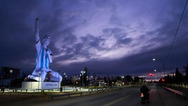 Eine Statue des Fußballstars Lionel Messi steht an einer Straße in Argentinien. Die Statue kniet und reißt den rechten Arm in die Luft.