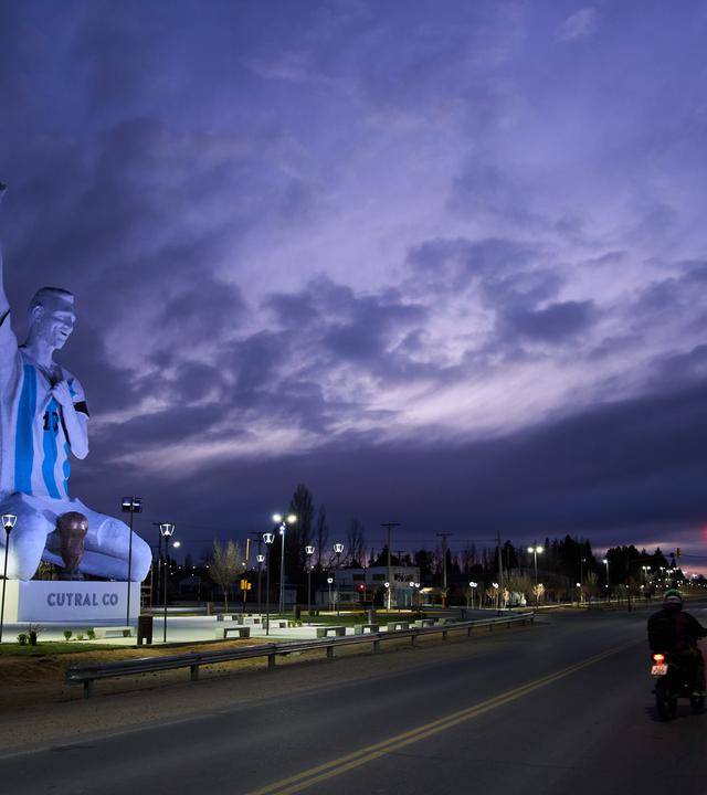 Eine Statue des Fußballstars Lionel Messi steht an einer Straße in Argentinien. Die Statue kniet und reißt den rechten Arm in die Luft.