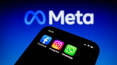 Die Apps von Facebook, Instagram und WhatsApp sind auf einem Smartphone vor dem Logo von Meta Platforms zu sehen.