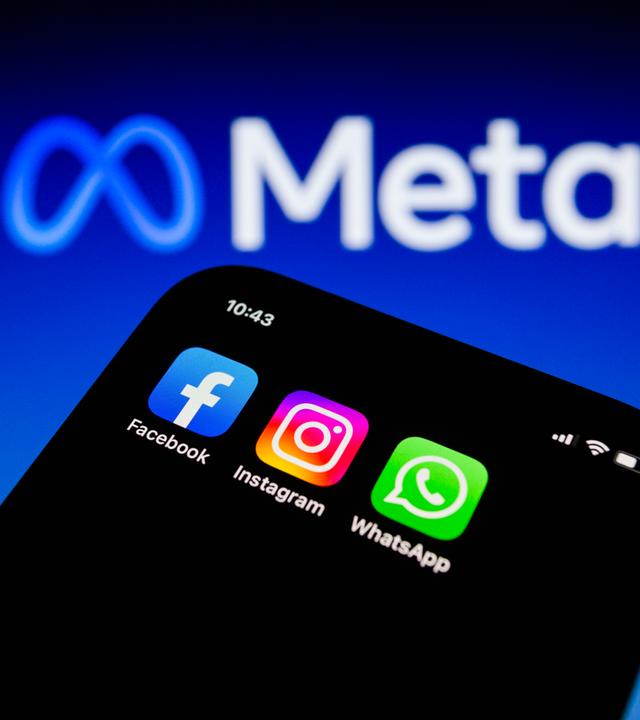Die Apps von Facebook, Instagram und WhatsApp sind auf einem Smartphone vor dem Logo von Meta Platforms zu sehen.