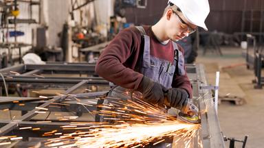 Junger Metallarbeiter schleift Stahl unter Funkenregen.