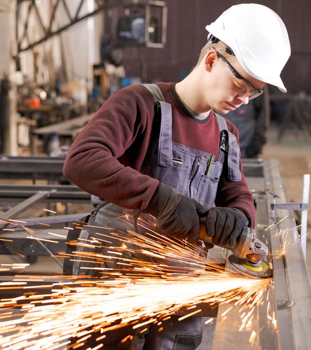 Junger Metallarbeiter schleift Stahl unter Funkenregen.