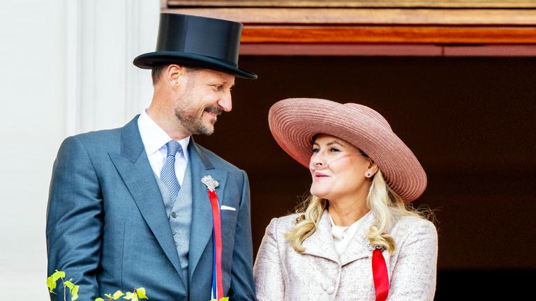 Mette Marit und Haakon schauen sich beim Nationalfeiertag 2026 auf dem Balkon an, Mette-Marit trägt ein Sauerstoffgerät.