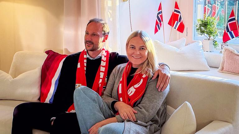 Mette-Marit und Haakon sitzen bei der WM gemeinsam auf dem Sofa, umgeben von Norwegen-Fahnen.