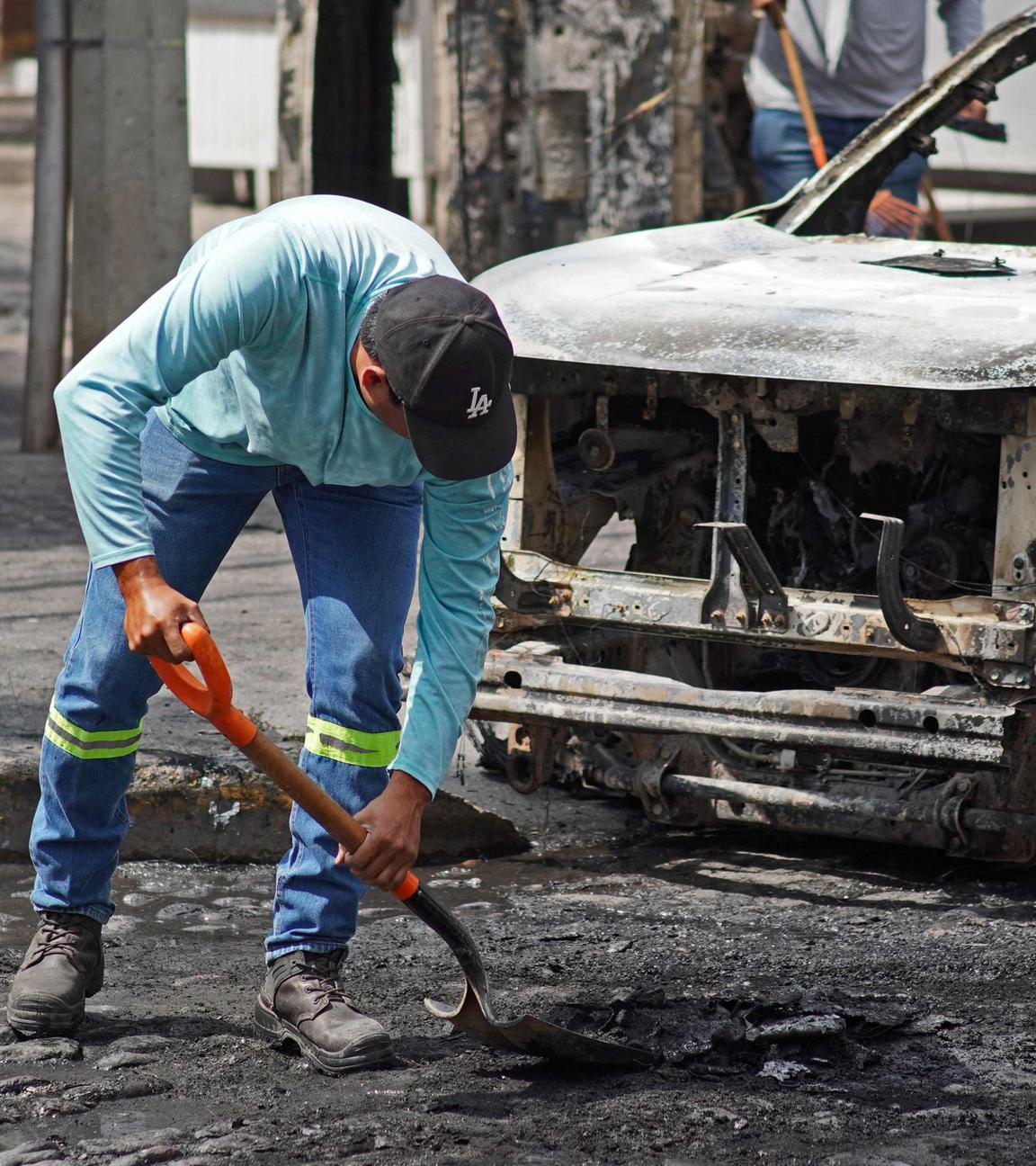 Ein Mann säubert die Straße vor einem ausgebrannten Auto