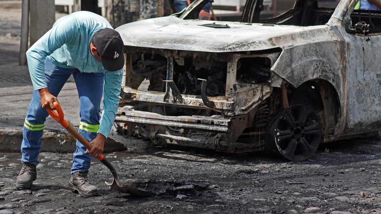 Ein Mann säubert die Straße vor einem ausgebrannten Auto