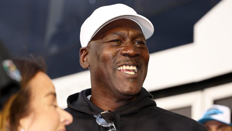 Michael Jordan trägt eine weiße Cap und lacht. 