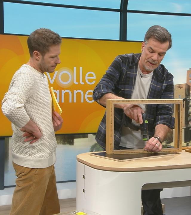 Mick Wewers bohrt in eine Regalwand. Florian Weiss schaut zu.