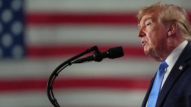 US-Präsident Donald Trump hält bei einer Wahlkampfveranstaltung in der Crossroads Arena eine Rede. Er steht seitlich zur Kamera und im Hintergund hängt die Flagge der USA
