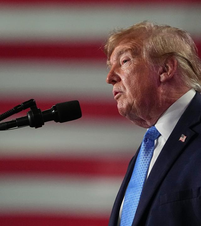 US-Präsident Donald Trump hält bei einer Wahlkampfveranstaltung in der Crossroads Arena eine Rede. Er steht seitlich zur Kamera und im Hintergund hängt die Flagge der USA