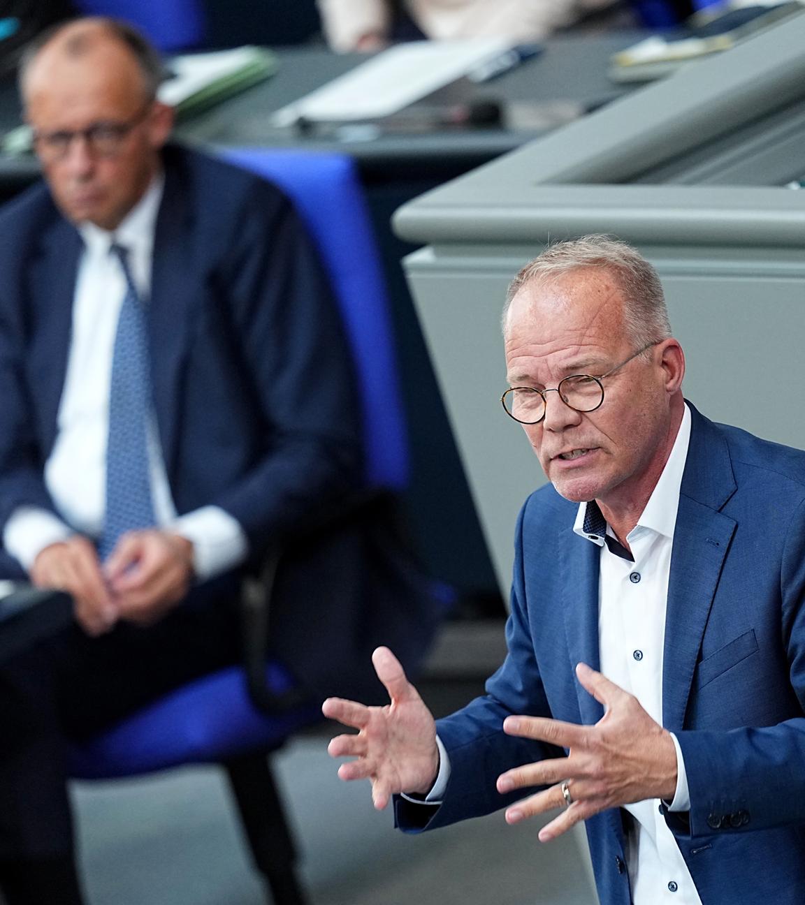 Matthias Miersch steht am Rednerpult im Bundestag. Im Hintergrund Bundeskanzler Merz mit eher ablehnendem Gesichtsausdruck.