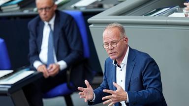 Matthias Miersch steht am Rednerpult im Bundestag. Im Hintergrund Bundeskanzler Merz mit eher ablehnendem Gesichtsausdruck.