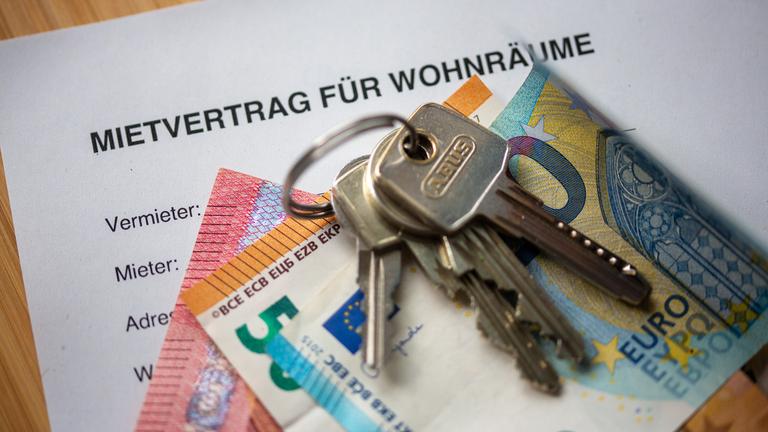 Auf einem ausgedruckten Mietvertrag liegen Geldscheine und ein Hausschlüssel.