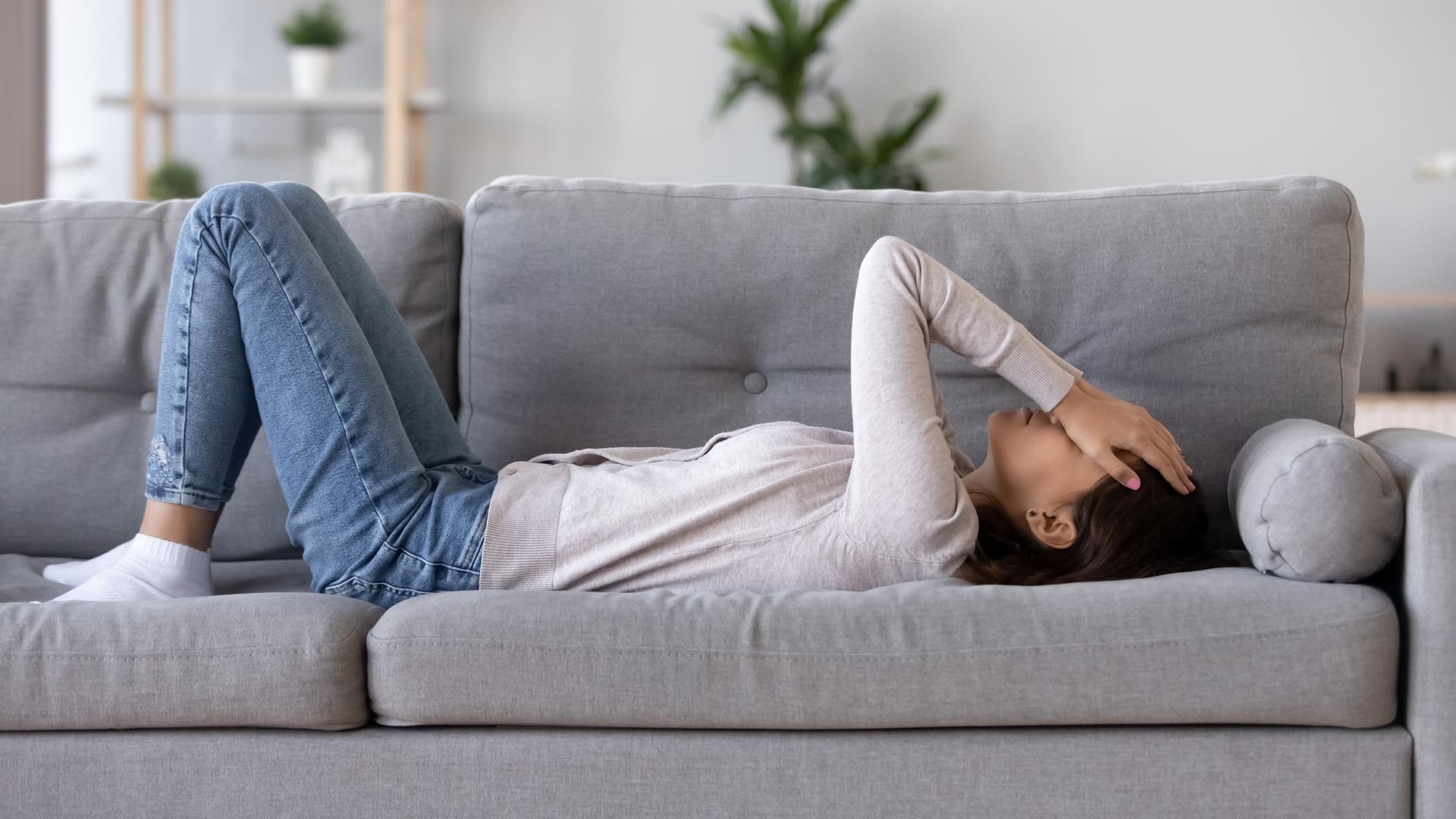 Junge Frau liegt mit Kopfschmerzen auf dem Sofa.