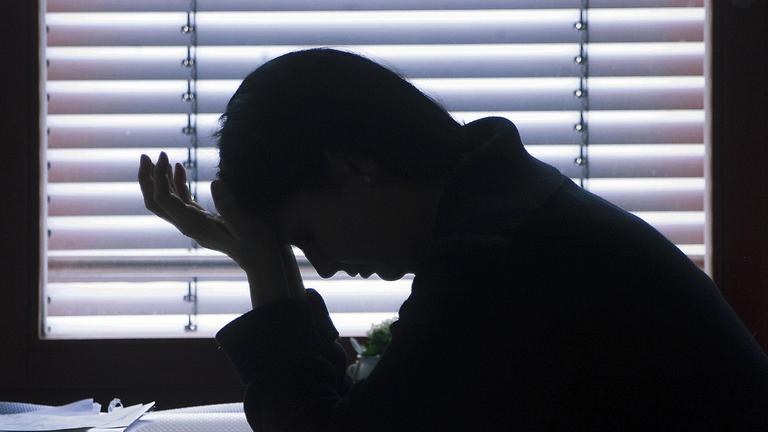 Es ist eine Frau zu sehen, wie sie am Schreibtisch sind und ihren Kopf in ihre Hände hält.