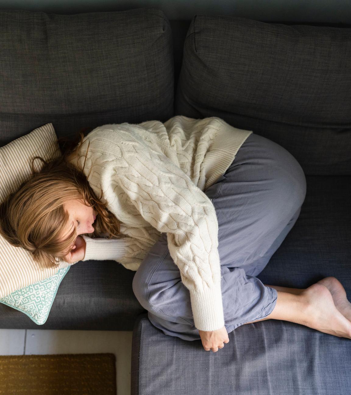 Woman with stomachache sleeping on sofa at home model released, Symbolfoto