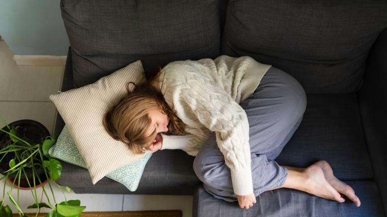Woman with stomachache sleeping on sofa at home model released, Symbolfoto