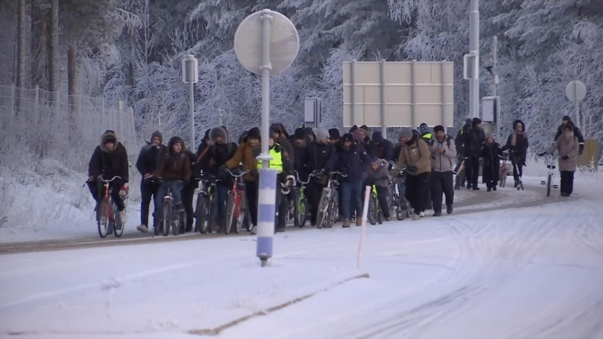 Gruppe von Migranten mit Fahrrädern gehen auf verschneiter Straße am russisch-finnischen Grenzübergang