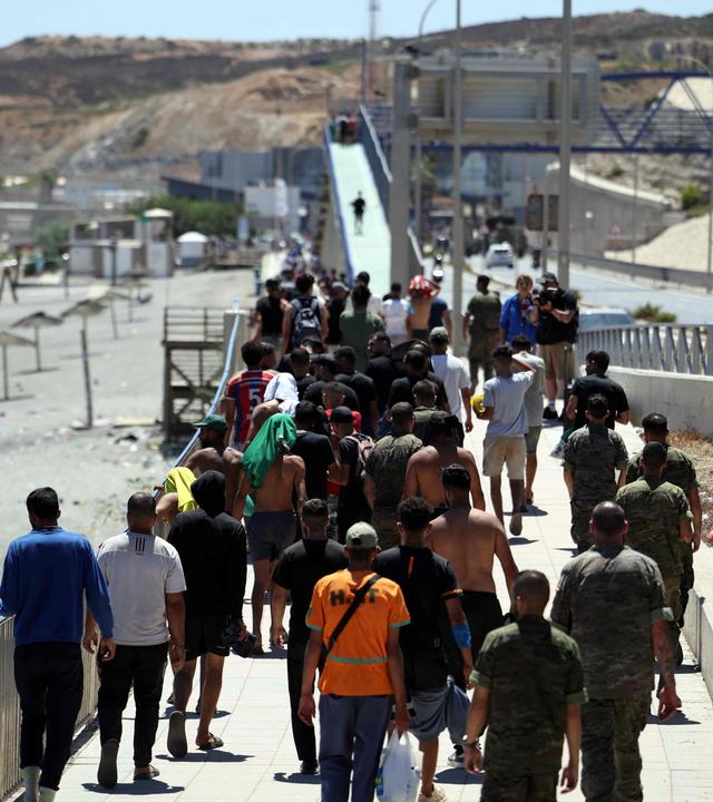Eine Gruppe von Migranten läuft unter Begleitung spanischer Infanteristen auf die marokkanische Grenze zu. 