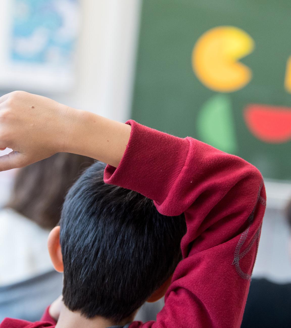Ein Kind mit rotem Pullover meldet sich im Schulunterricht.
