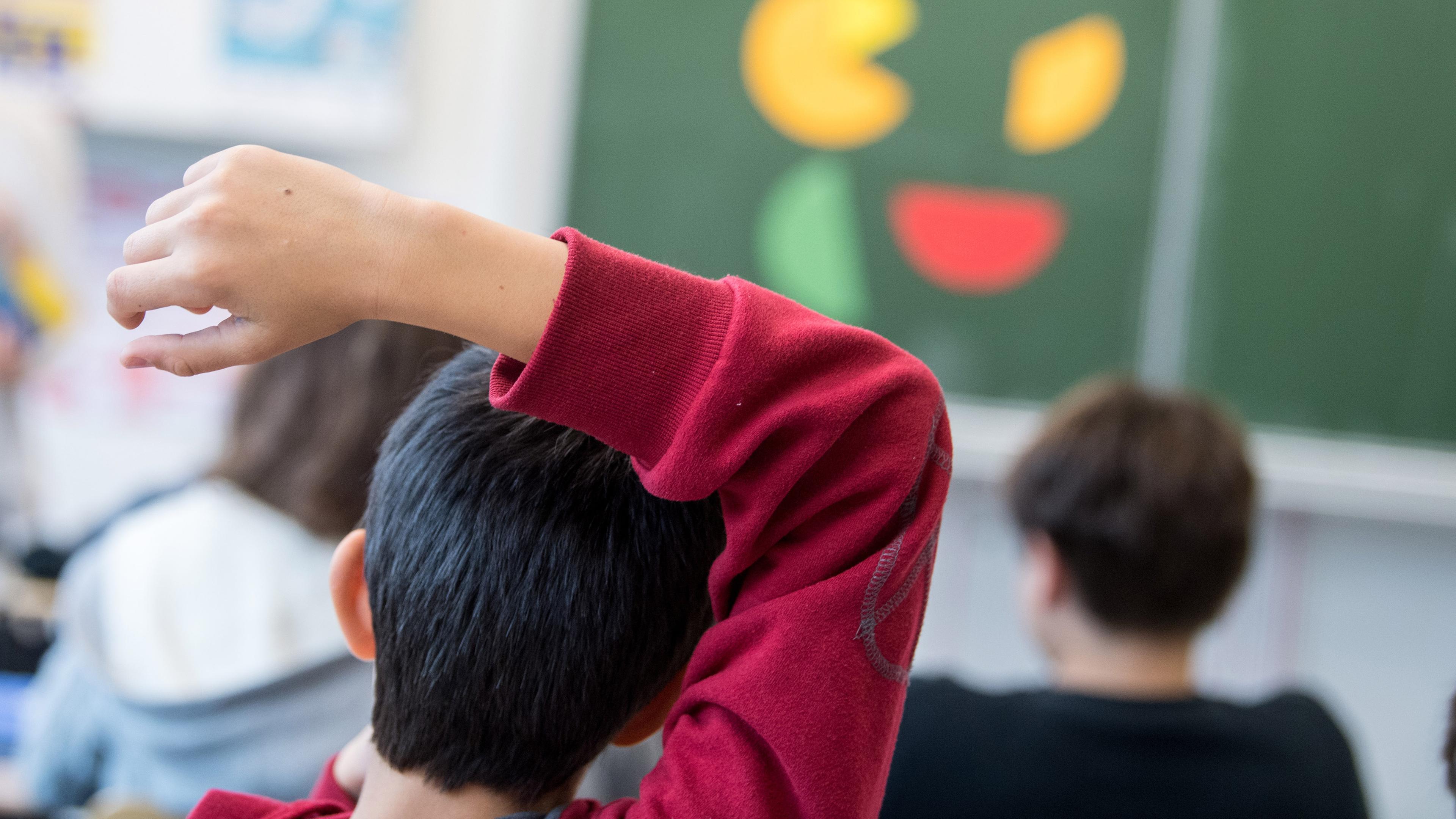 Ein Kind mit rotem Pullover meldet sich im Schulunterricht.
