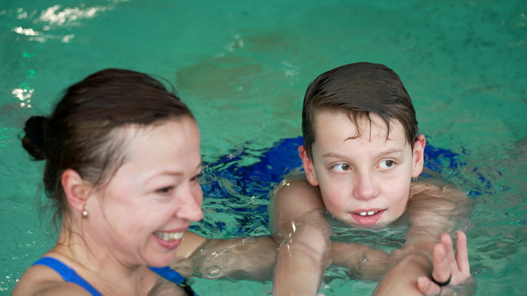 Mima Heldin Veronika im Wasser mit einem Kind, dem sie schwimmen beibringt