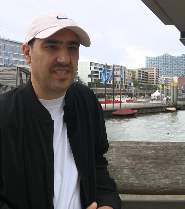 Homayoon Pardis steht auf einer Brücke in Hamburg und spricht.