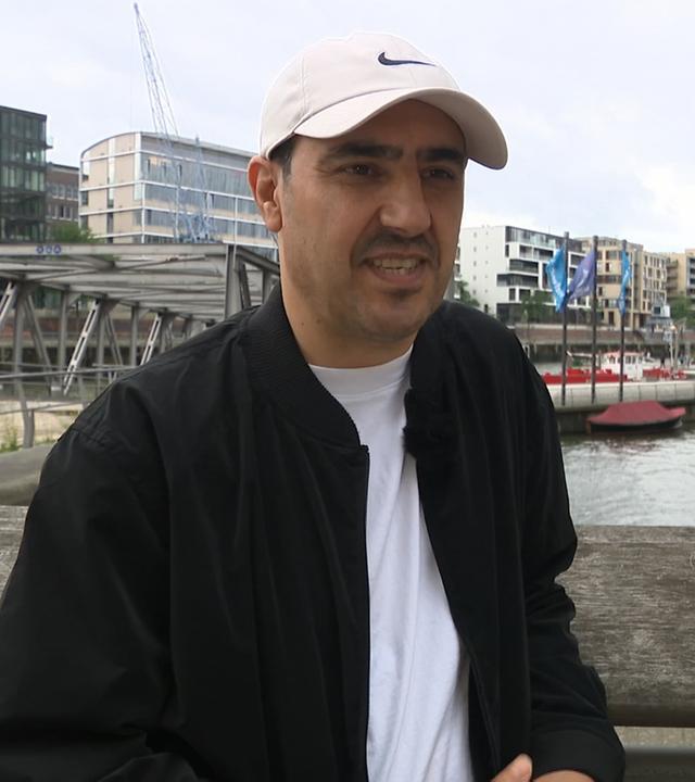 Homayoon Pardis steht auf einer Brücke in Hamburg und spricht.