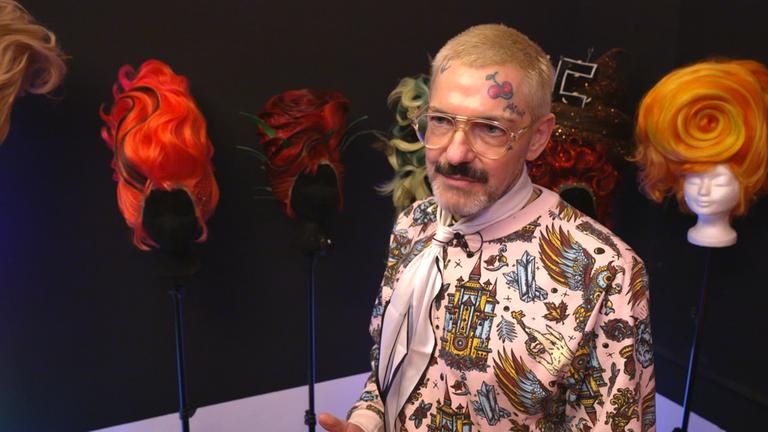 Mima-Mensch Karl Gadzali vor seinen extravaganten, bunten Perücken 