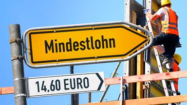Ansteigender Wegweiser mit Aufschrift Mindestlohn vor Baustelle