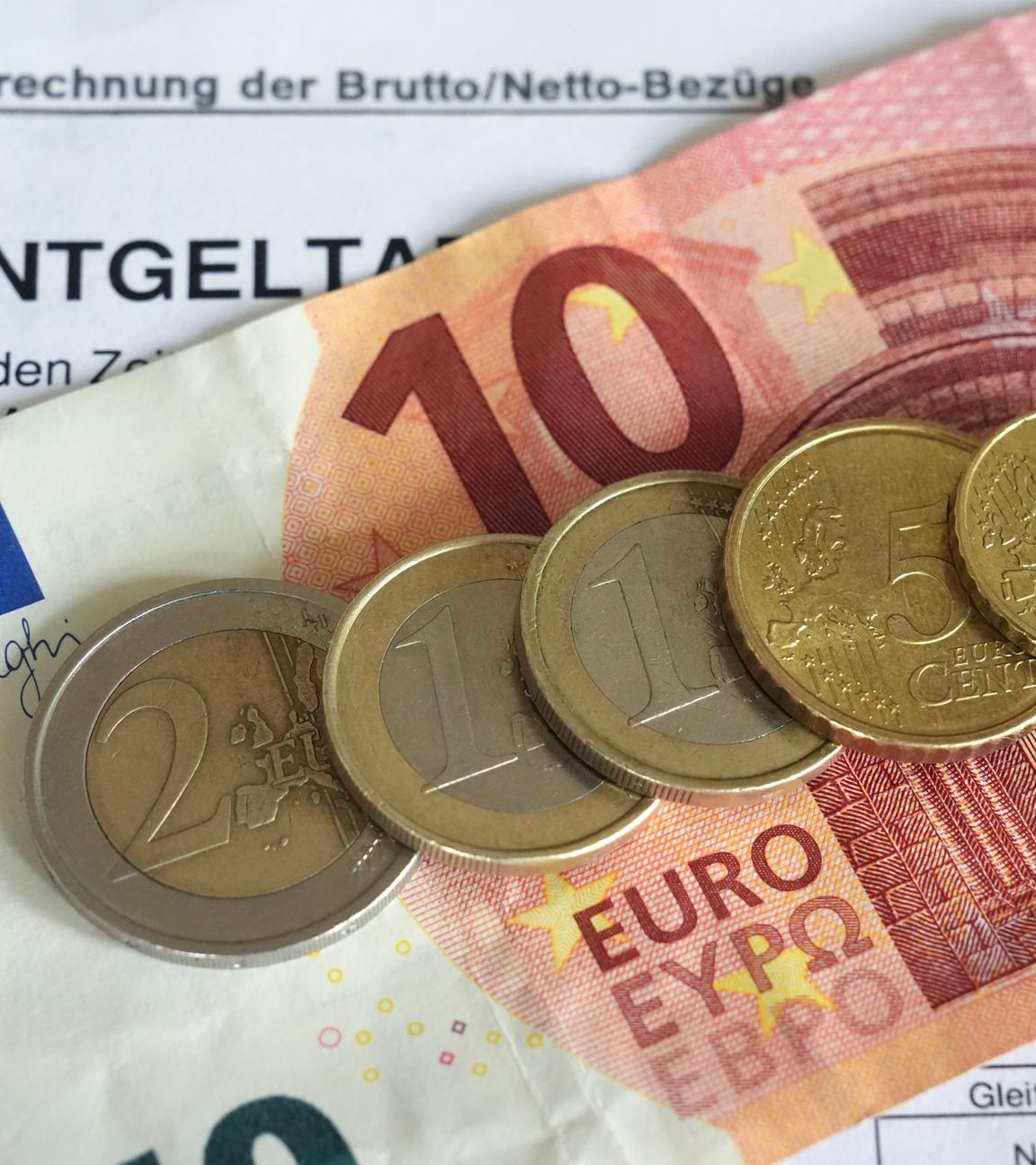 Euro- und Centmünzen liegen auf einer Entgeltabrechnung und auf einem 10-Euro-Schein und bilden mit diesem zusammewn die Summe von 14,60 Euro. Der Mindestlohn in Deutschland soll in zwei Stufen auf 14,60 Euro zum 1. Januar 2027 steigen.