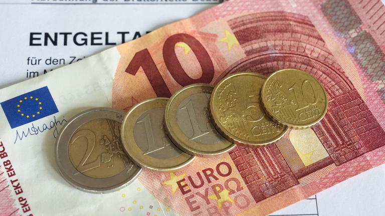 Euro- und Centmünzen liegen auf einer Entgeltabrechnung und auf einem 10-Euro-Schein und bilden mit diesem zusammewn die Summe von 14,60 Euro. Der Mindestlohn in Deutschland soll in zwei Stufen auf 14,60 Euro zum 1. Januar 2027 steigen.